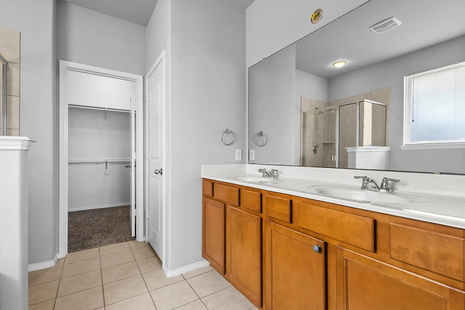 Bathroom featuring a double vanity with wood cabinetry, a large wall-mounted mirror, and tile flooring