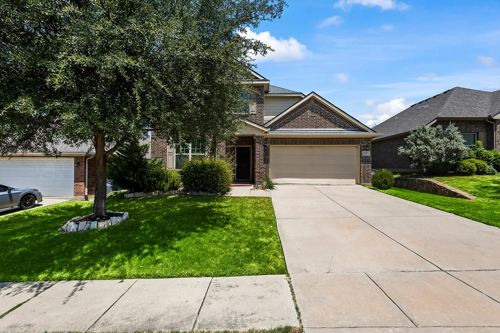 Brick facade property featuring a two-car garage, concrete driveway, and established landscaping