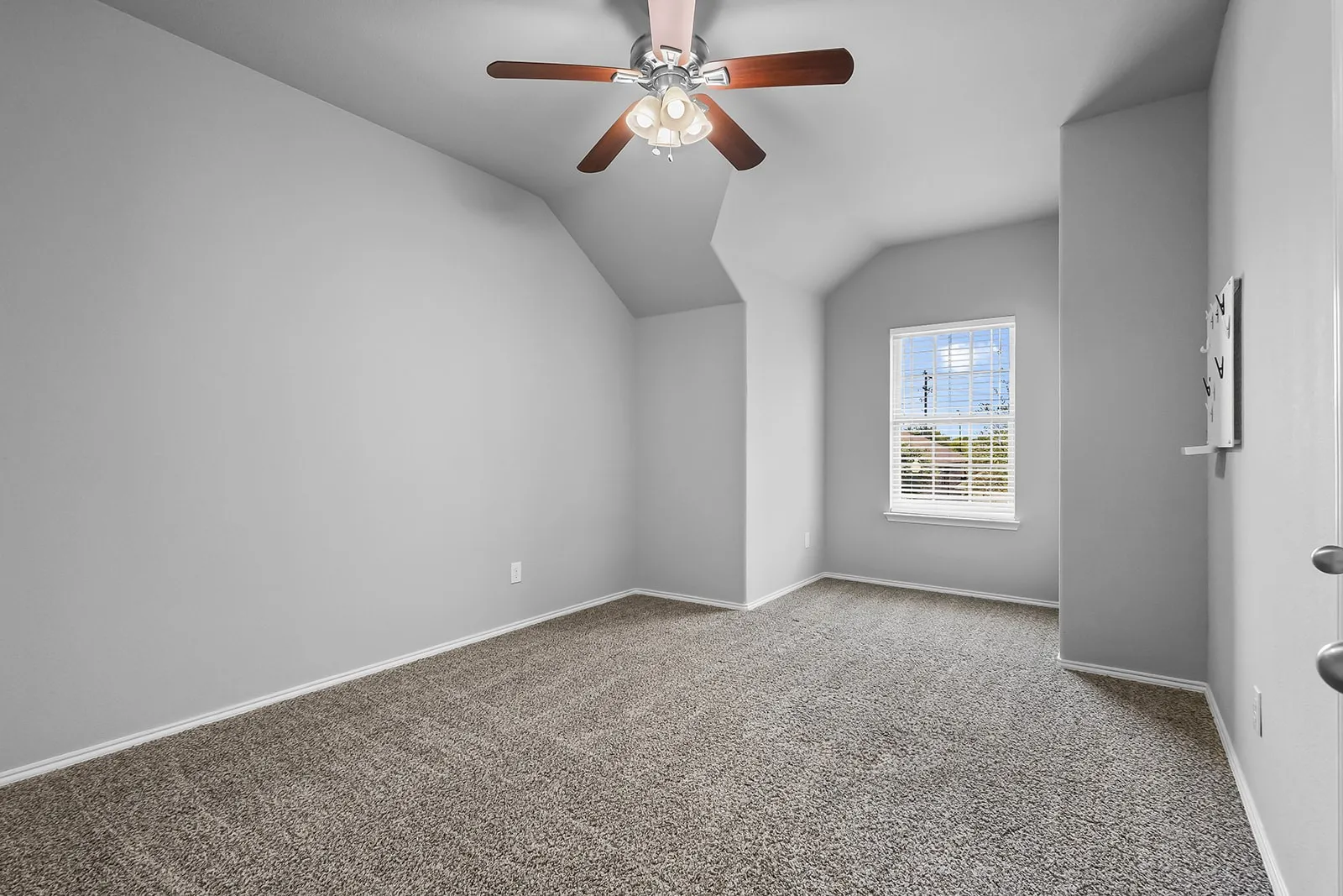 Carpeted room featuring a ceiling fan with wood-finish blades, a single window with blinds, and light gray walls