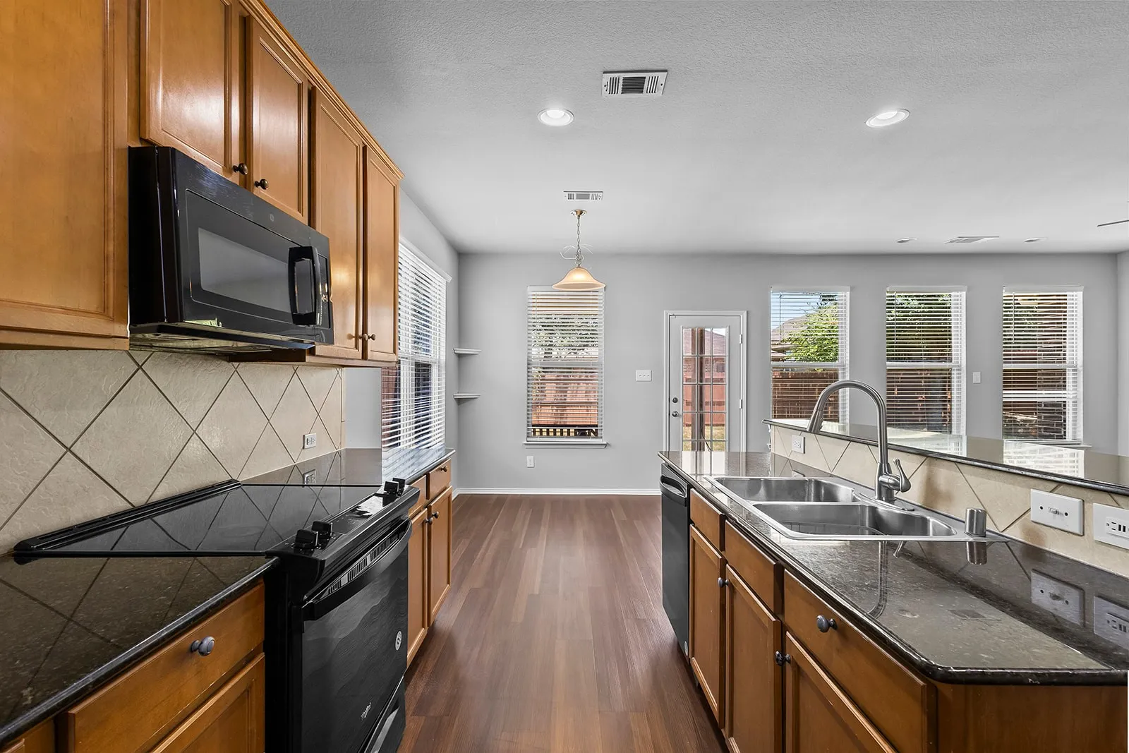 Galley-style kitchen featuring warm wood cabinetry, black stainless steel appliances, geometric tile backsplash, and gray quartz countertops