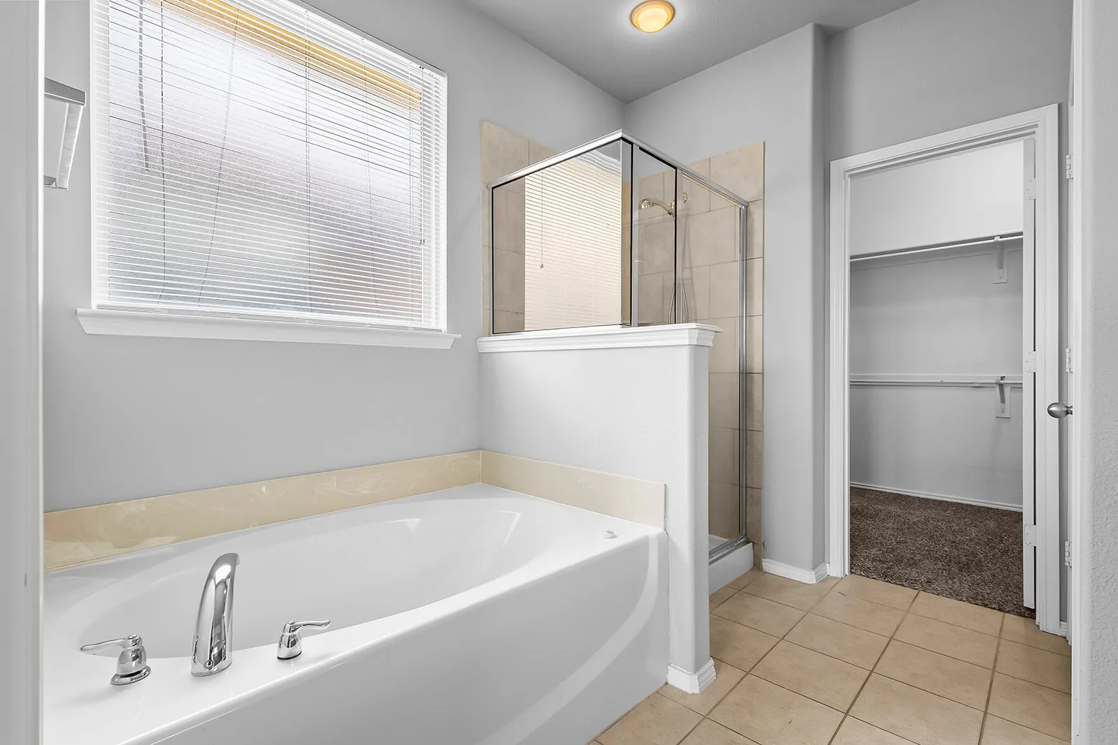 Soaking tub with polished chrome fixtures, tile flooring, and a separate shower enclosure with glass doors