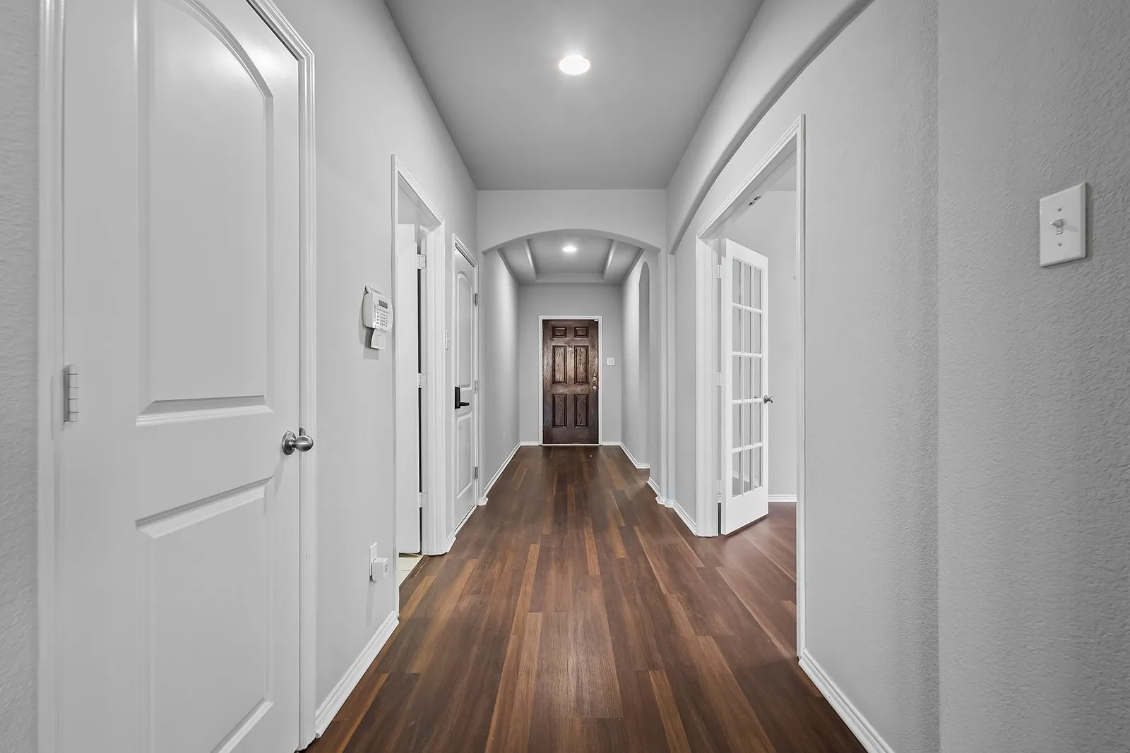 Hallway featuring wood-finish flooring, light gray walls, white trim, recessed lighting, and an arched doorway