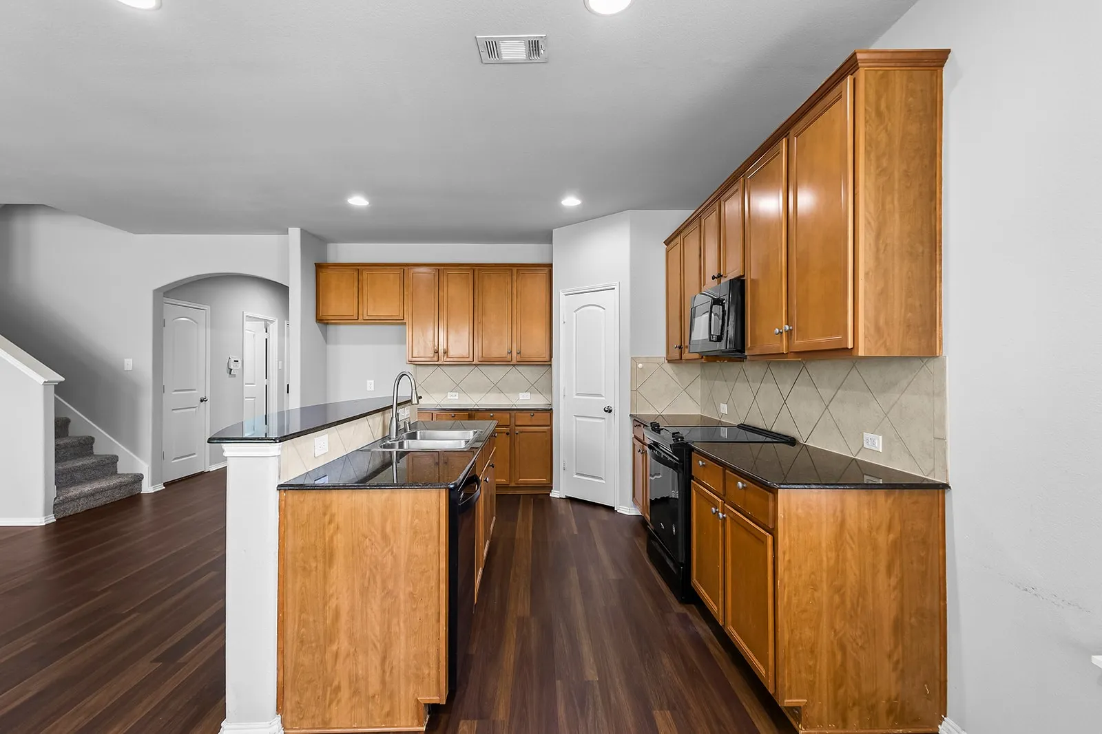 Kitchen featuring wood-finish cabinetry, black countertops, and a tile backsplash