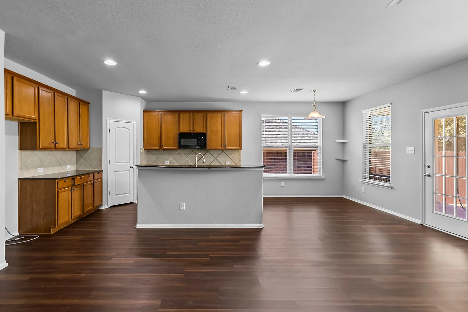 Expansive open-concept living area featuring wood-finish flooring, ample natural light, recessed lighting, and a well-appointed kitchen with wood cabinetry and dark countertops