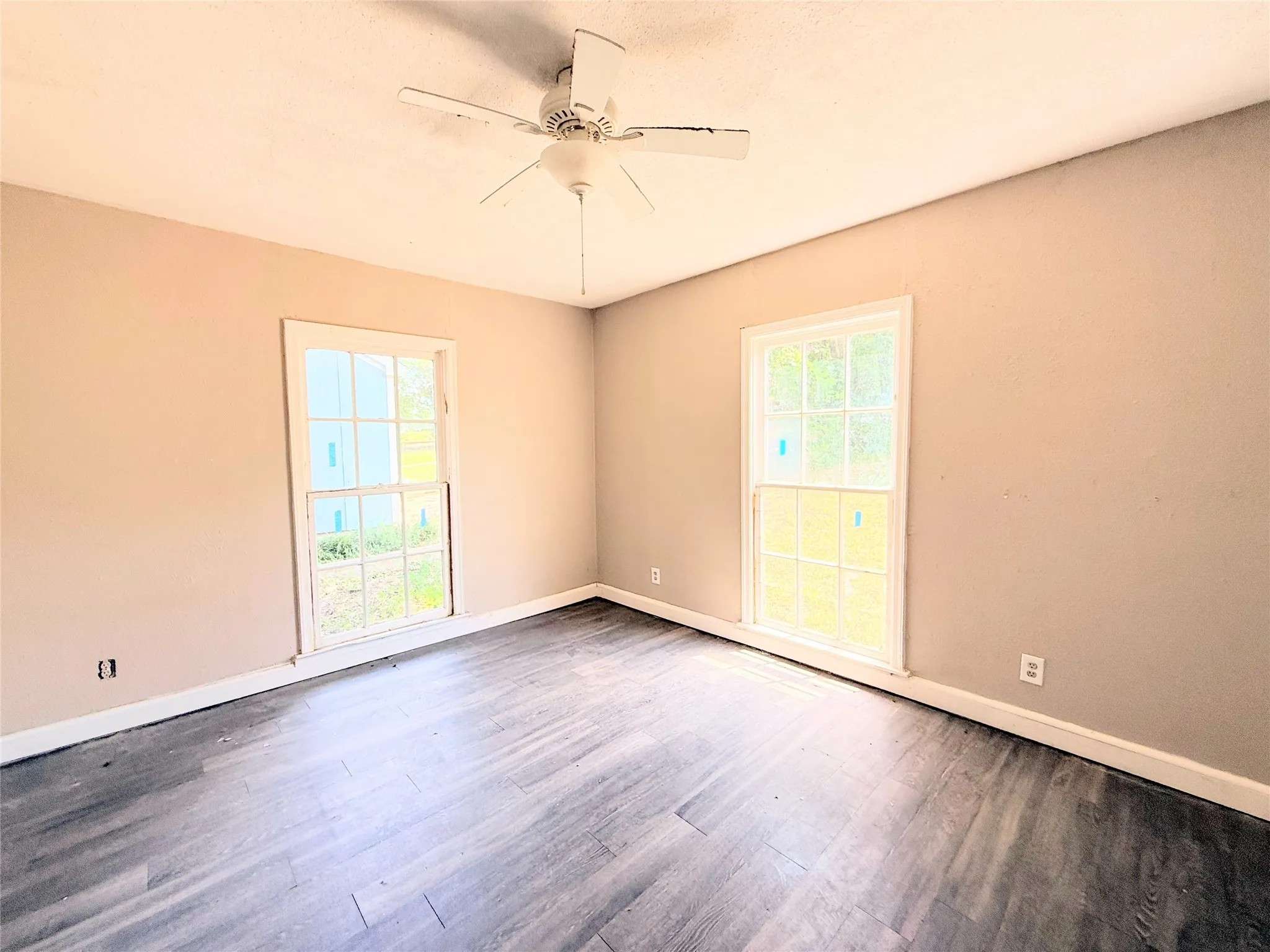 Room with wood-finish flooring, two window openings, and a ceiling fan
