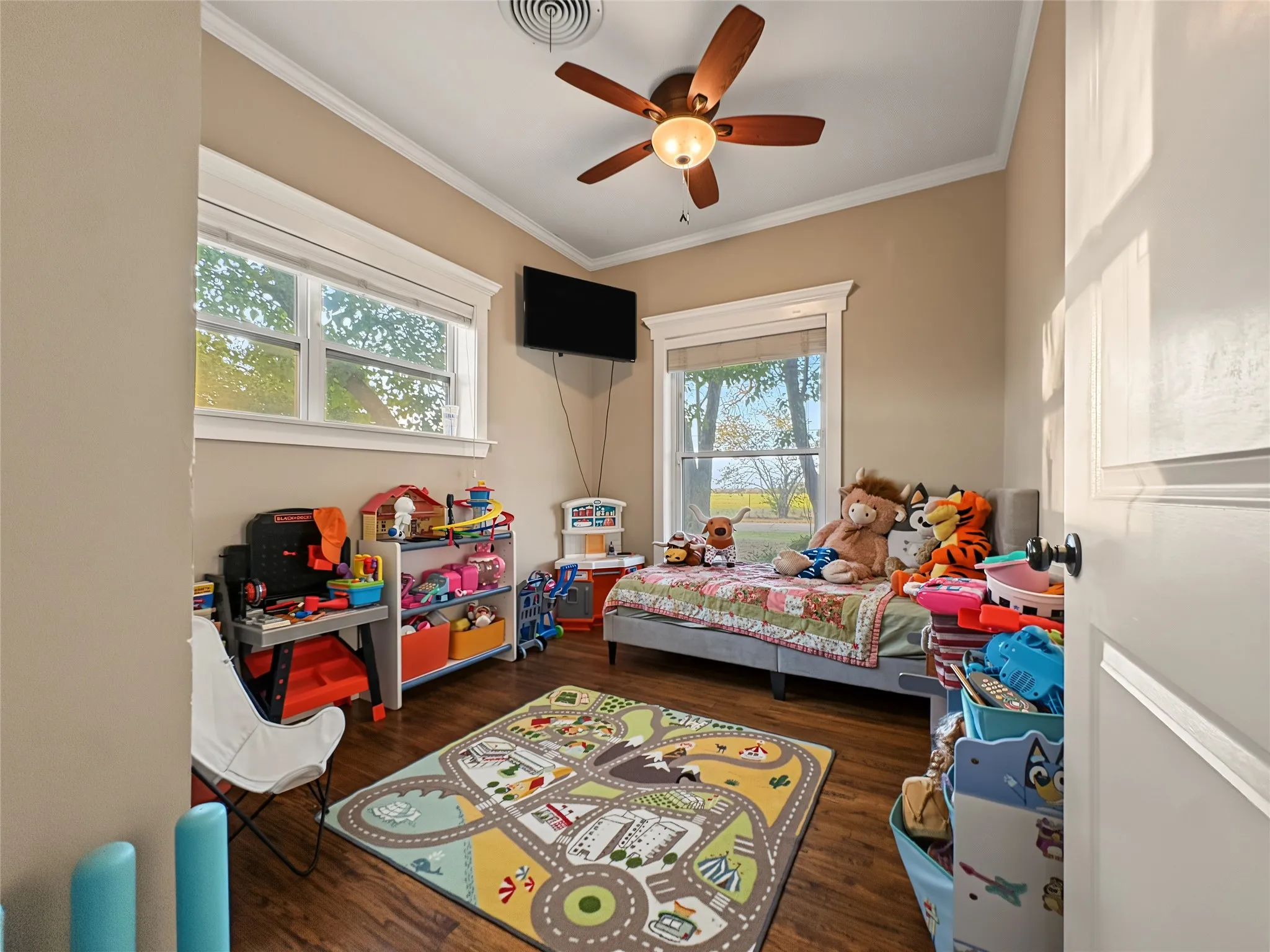Wood-finish flooring, two large windows, ceiling fan with integrated lighting, and crown molding