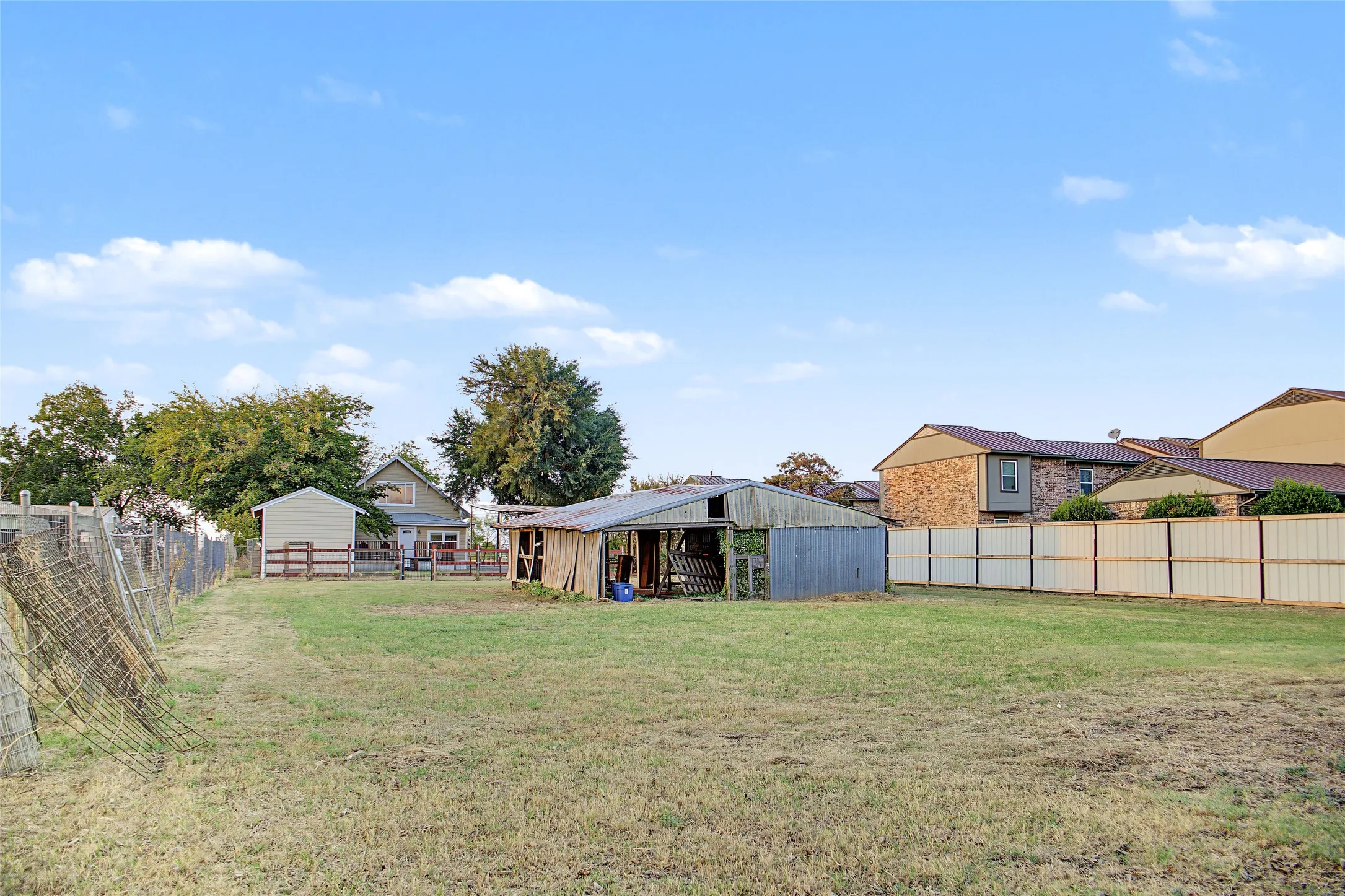 Expansive grassy lot featuring a metal fence, wood fencing, and a detached shed