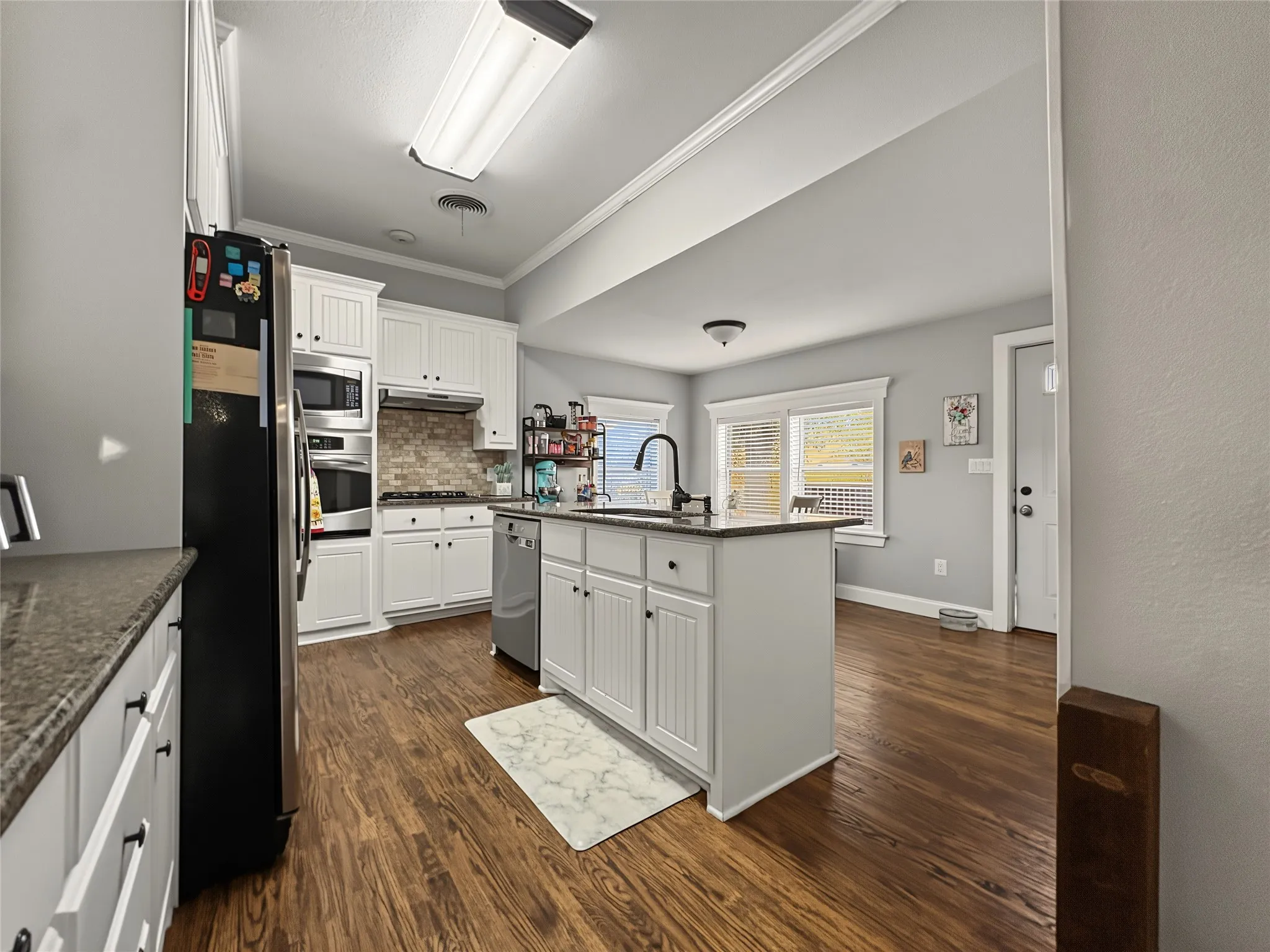 Kitchen featuring white cabinetry, dark stone countertops, wood-finish flooring, a central island with a sink, and stainless steel appliances