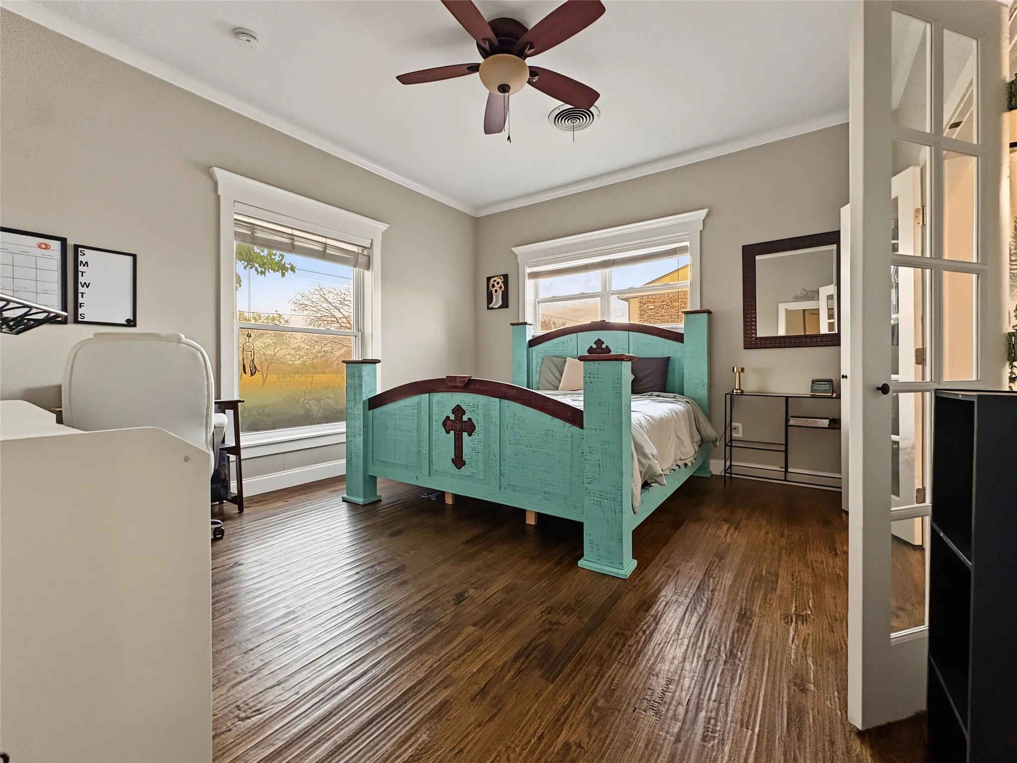Wood-finish flooring, crown molding, double windows with trim, ceiling fan, and French doors