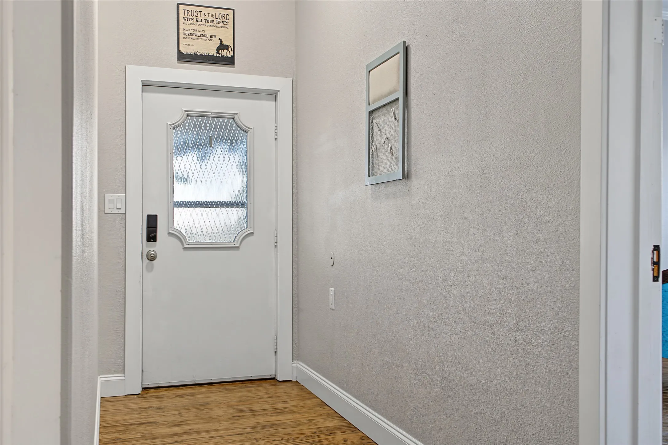 White entry door with decorative glass insert, dark hardware, and wood-finish flooring