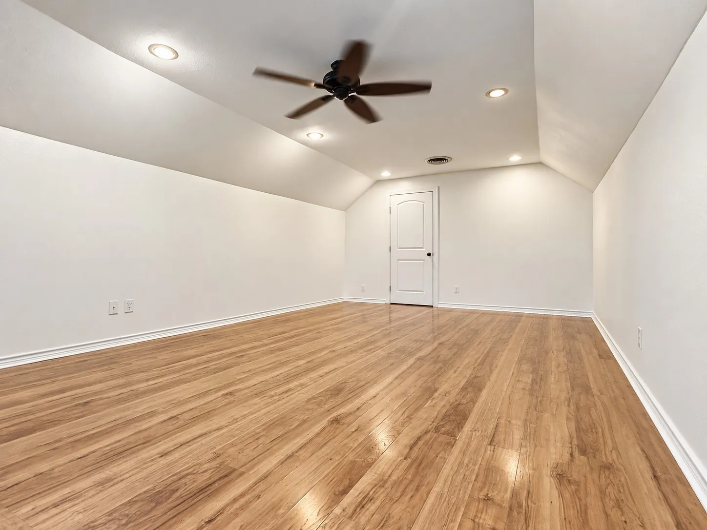 Wood-finish flooring, recessed lighting, ceiling fan, white paneled door, and angled ceilings