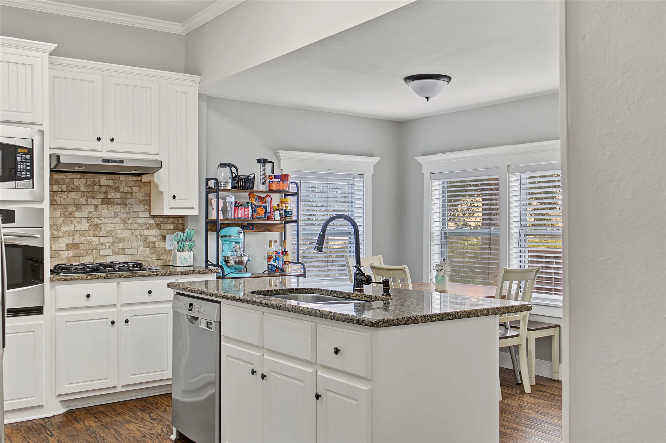 Kitchen featuring white cabinetry, granite countertops, stainless steel appliances, a tiled backsplash, and wood-finish flooring