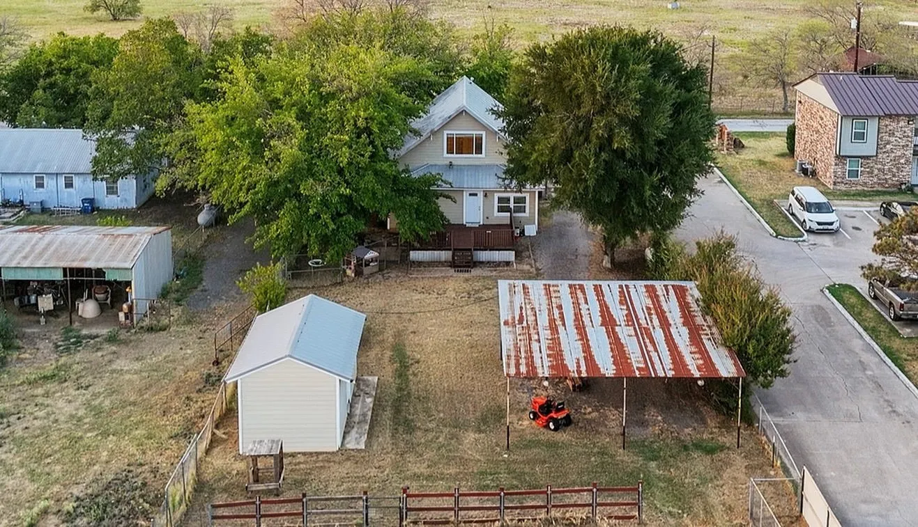 Detached metal-sided shed with a pitched roof, additional open-sided metal structure, and a fenced perimeter