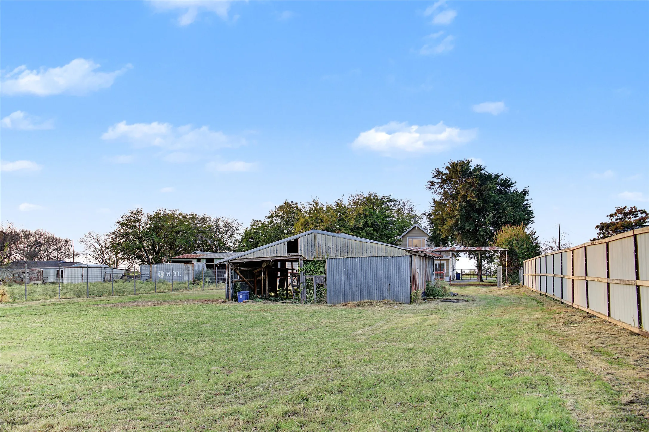 Expansive grassy yard with a wooden-sided barn structure, chain-link fencing, and a tall privacy fence