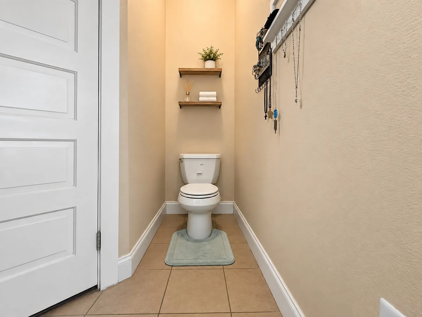 Recessed toilet area featuring ceramic tile flooring and two wall-mounted wooden shelves