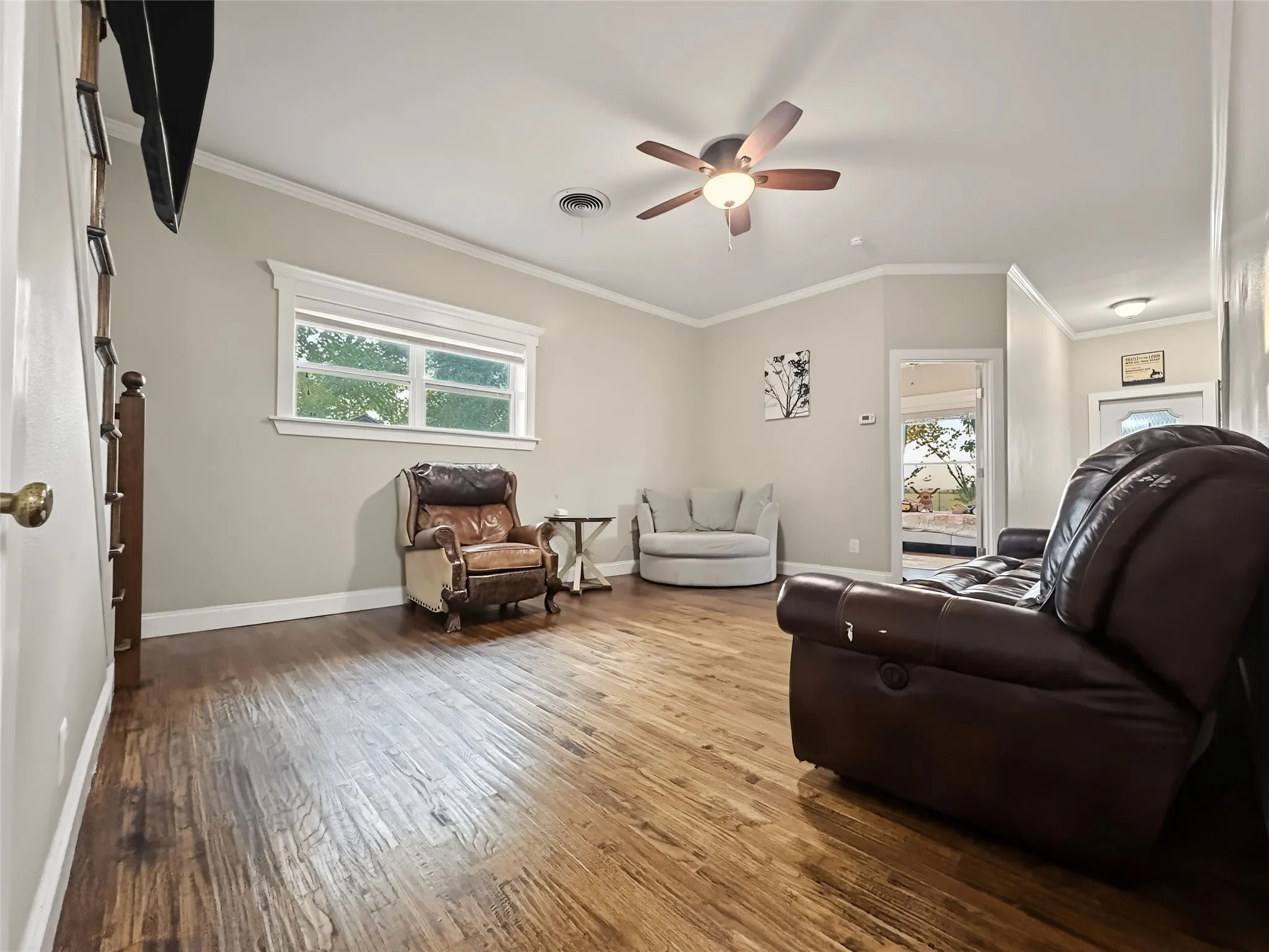Wood-finish flooring, vaulted ceiling, crown molding, ceiling fan, and window with white trim