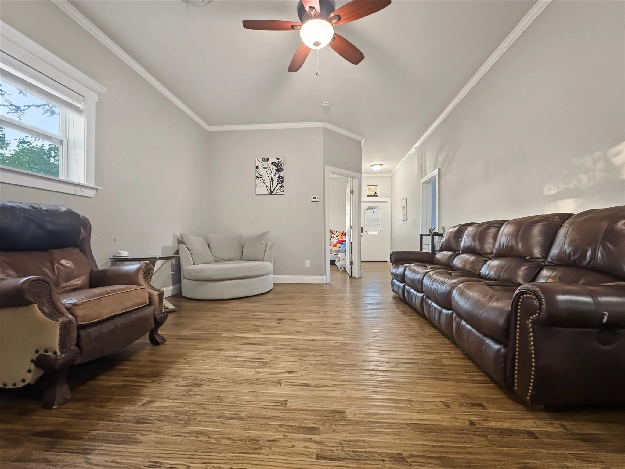 Wood-finish flooring throughout, ceiling fan with integrated lighting, and crown molding accents