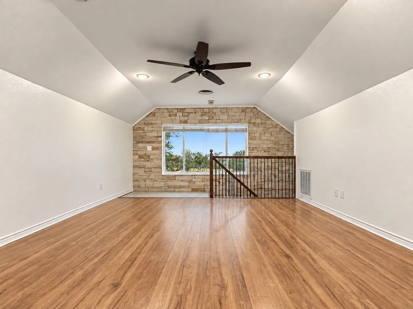 Spacious room with wood-finish flooring, stone accent wall, ceiling fan, recessed lighting, and a window with natural light