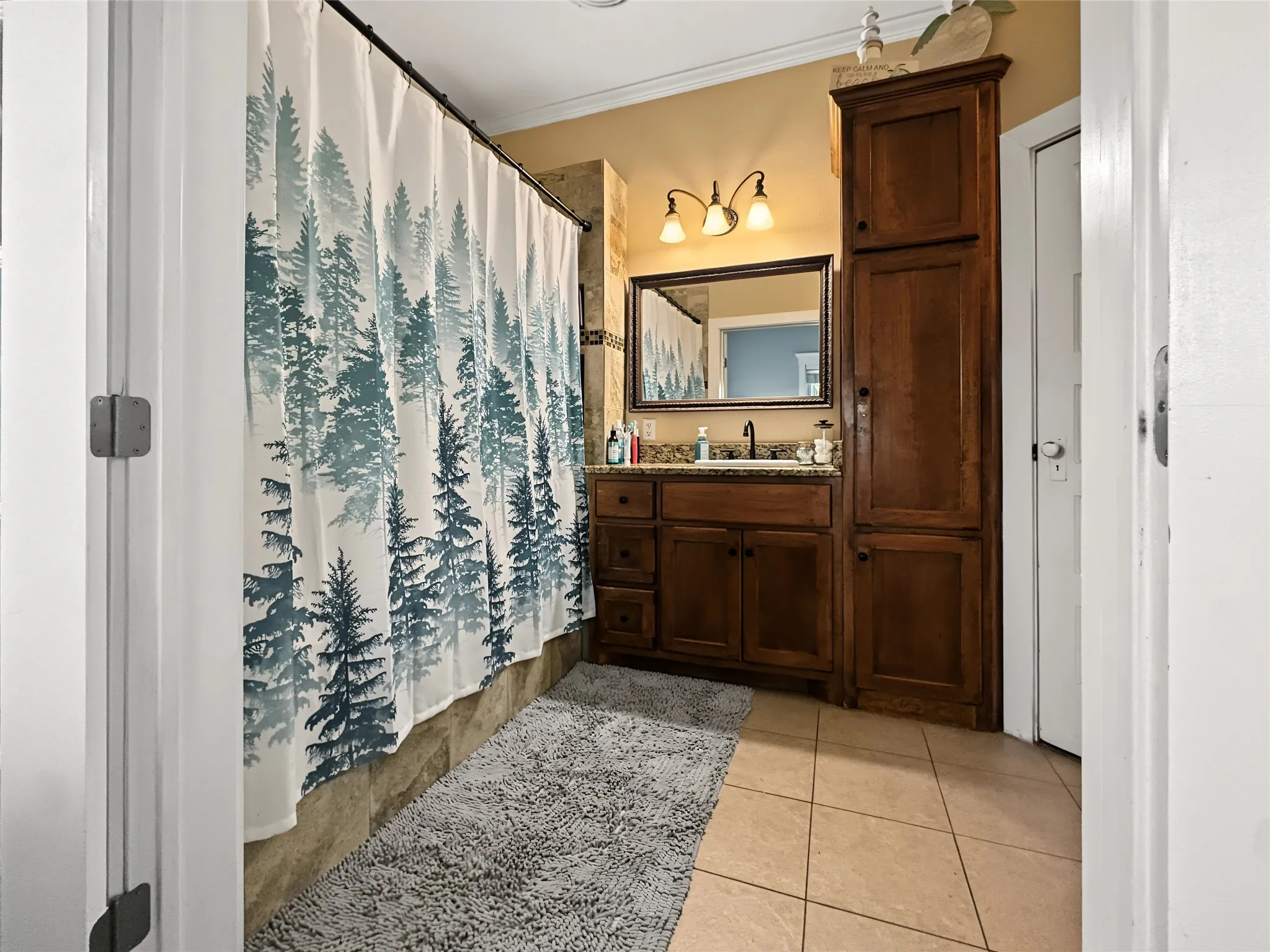 Warm-toned tile flooring, wood-finish vanity with a built-in sink, and a wall-mounted mirror