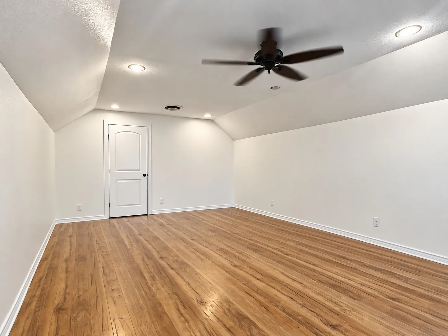 Vaulted ceiling with a ceiling fan and recessed lighting, wood-finish flooring, and white paneled door