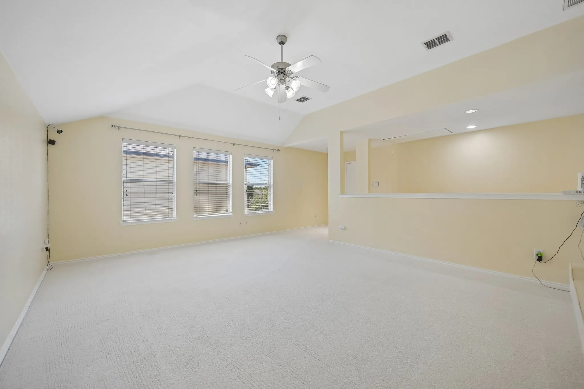 Vaulted ceiling with ceiling fan, three horizontal windows with blinds, recessed lighting, and light-colored carpeting