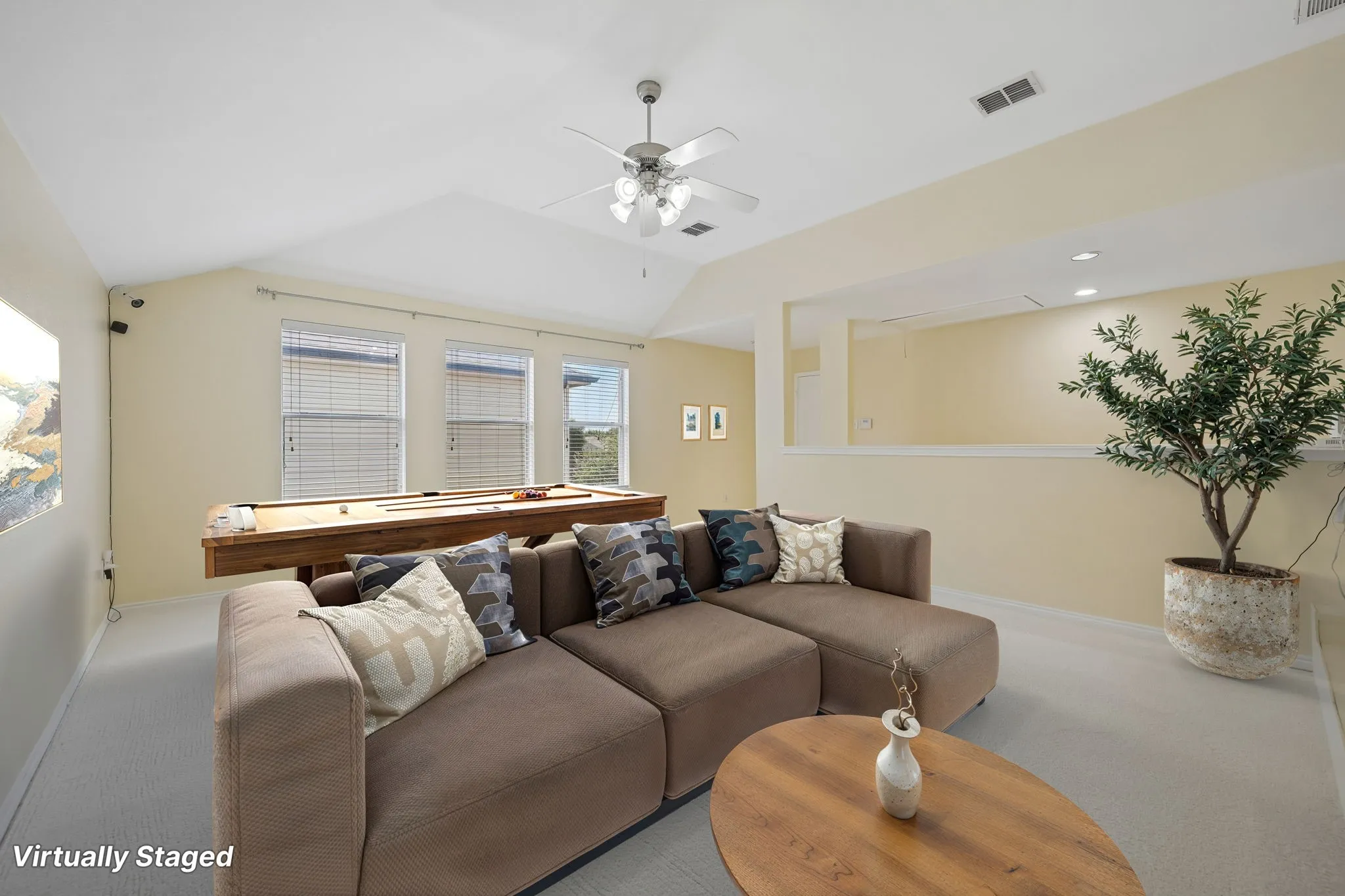 VIRTUALLY STAGED Bright and airy living space showcasing vaulted ceilings with ceiling fan, multiple windows with natural light, warm neutral wall finishes, wood-finish flooring, and a built-in planter accent