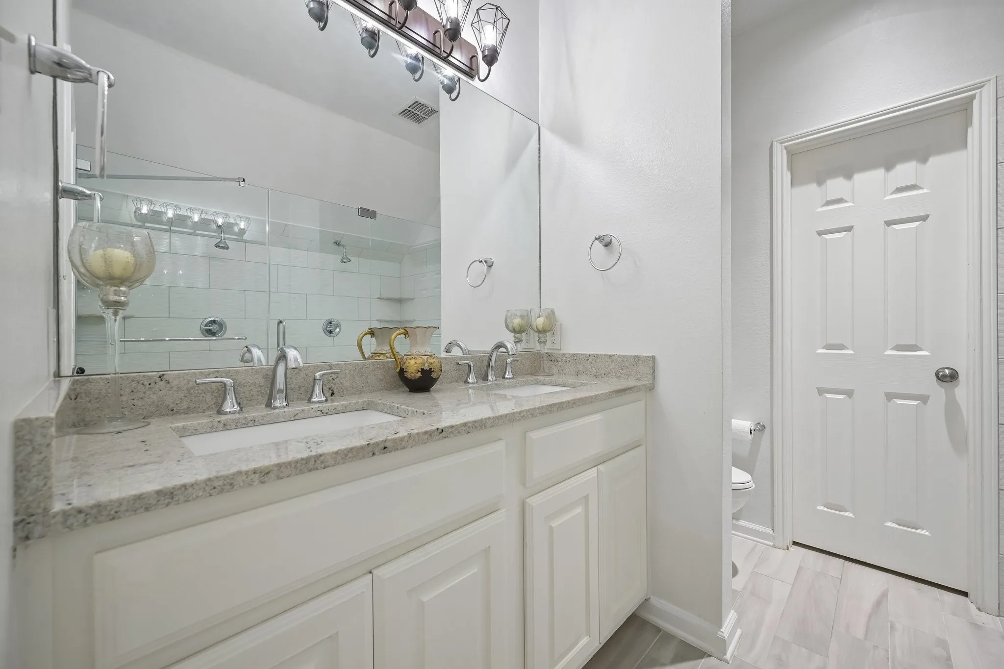 Dual vanity with integrated sinks, granite countertop, chrome fixtures, and white cabinetry