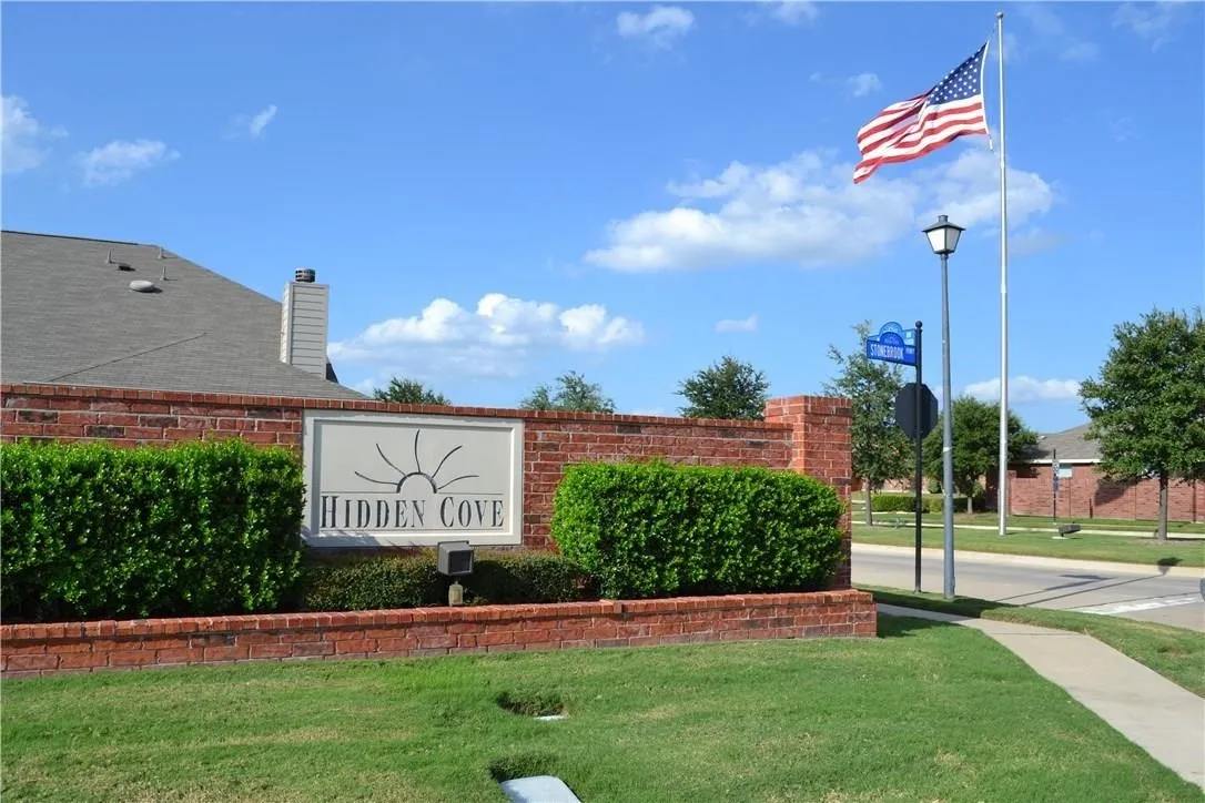 Brick entryway wall with a stone sign, manicured shrubs, a street light, and a sidewalk