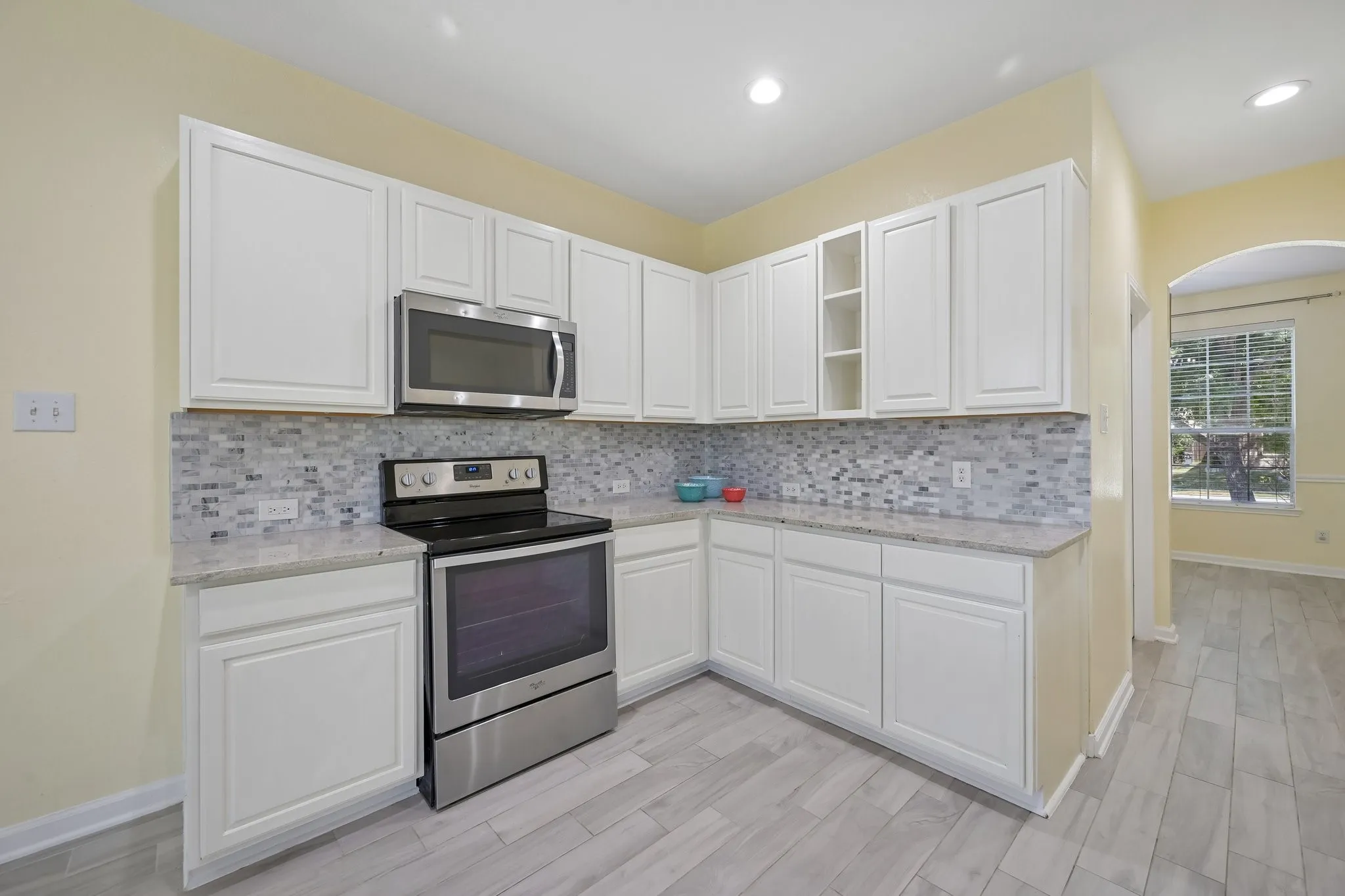 Kitchen featuring white cabinetry, granite countertops, tile backsplash, stainless steel range, and wood-finish flooring