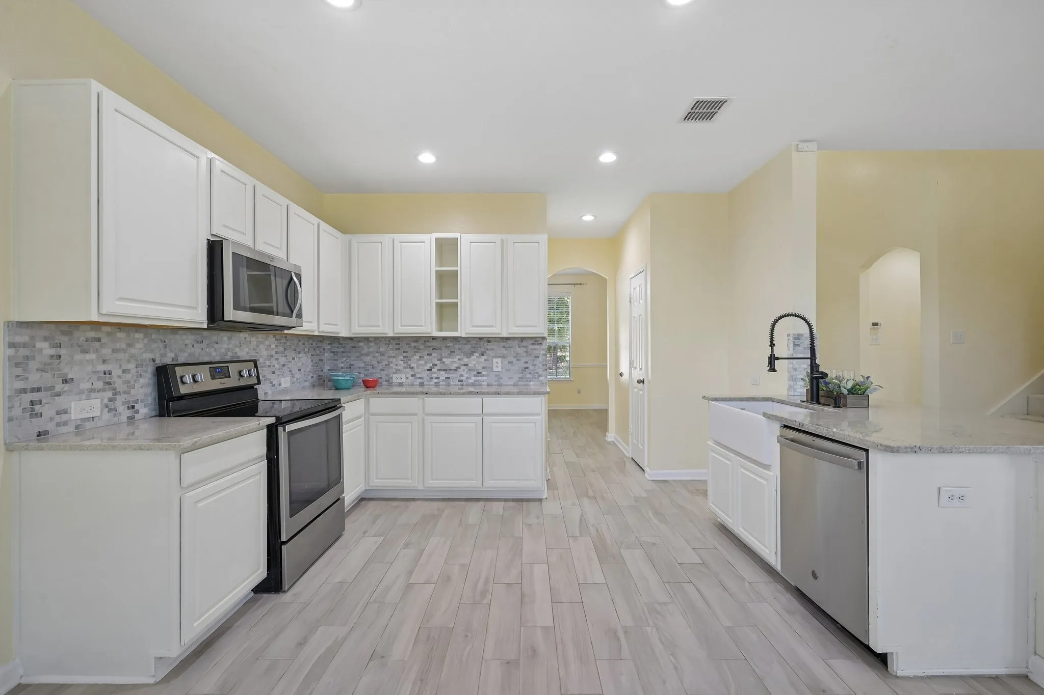 Kitchen featuring white cabinetry, light-toned countertops, tile backsplash, wood-look tile, and stainless steel appliances