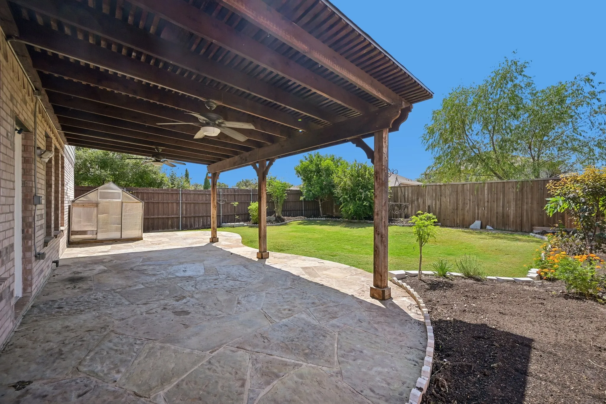 Expansive covered patio with flagstone flooring, wood ceiling with integrated fans, and wood support beams