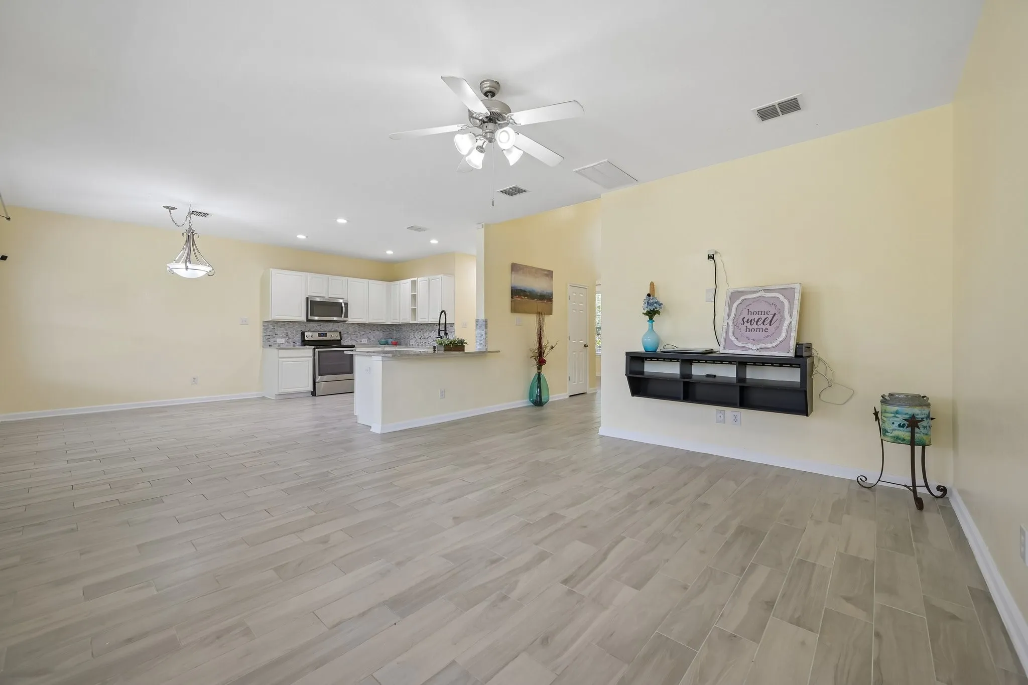 Spacious interior with tile flooring, featuring a kitchen with white cabinetry, stainless steel appliances, and a tiled backsplash
