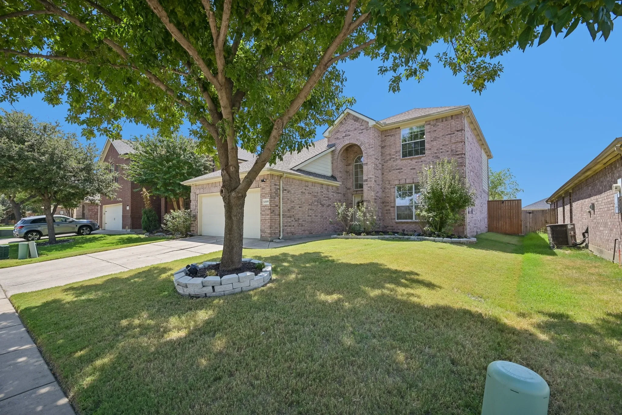 Brick facade with an arched entry window, dual garage doors, and a landscaped front yard with a mature tree