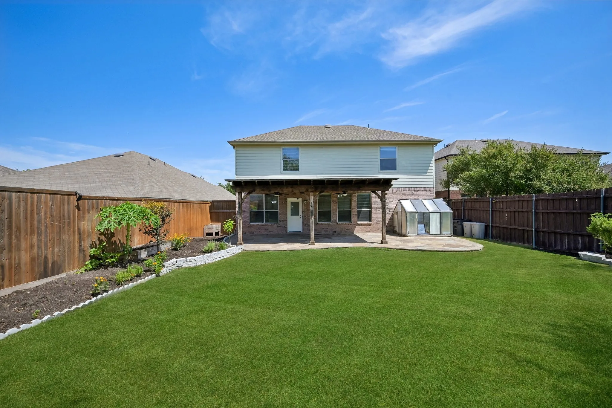 Expansive backyard featuring a manicured lawn, a covered patio with a wooden pergola, and a raised garden bed with stone edging