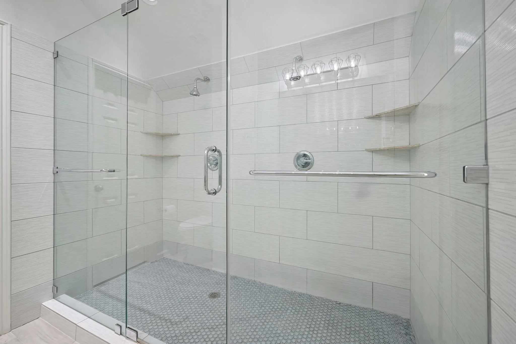 Glass-enclosed shower with a rainfall showerhead, integrated corner shelving, and a mosaic tile floor