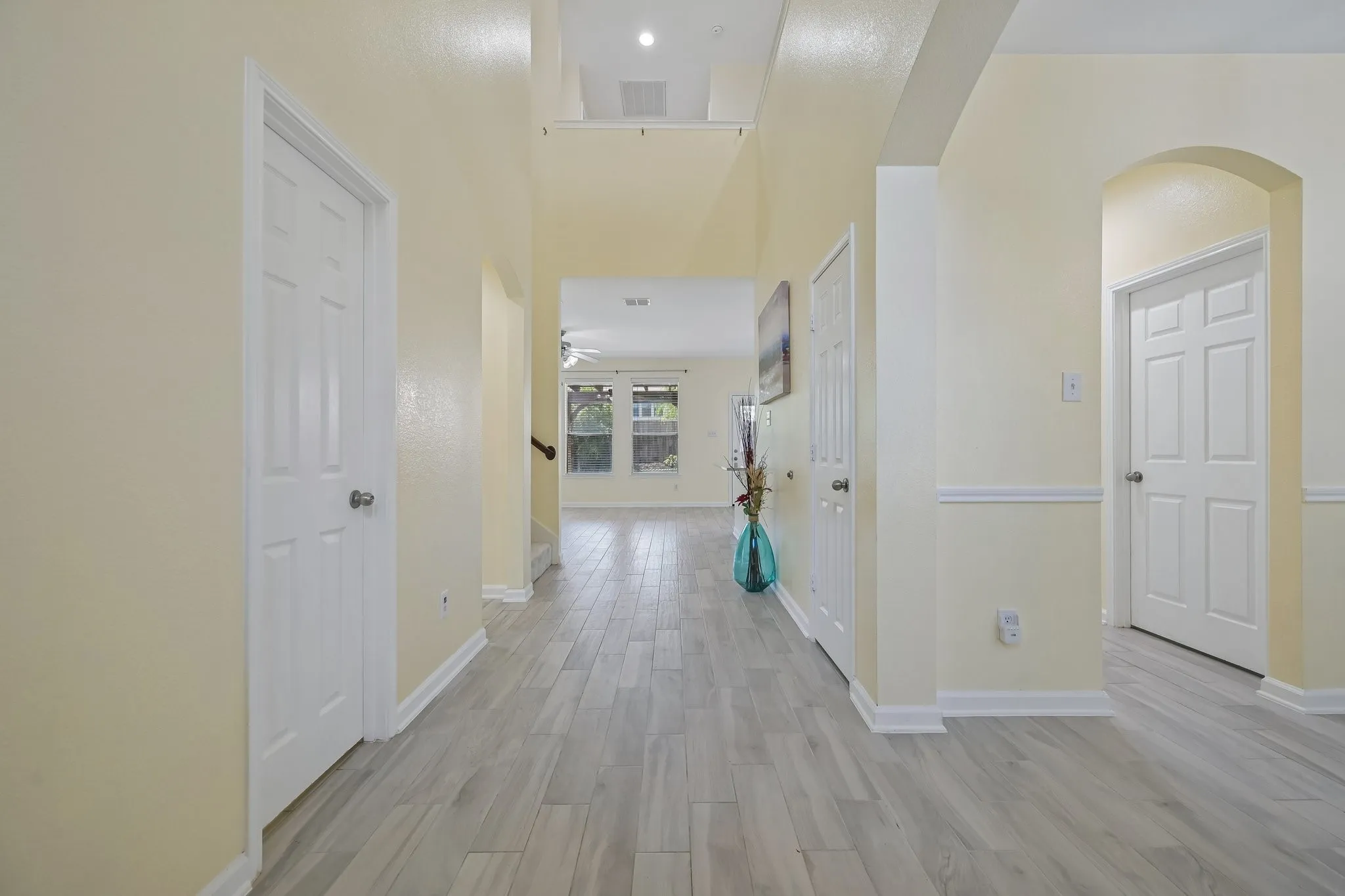 Bright hallway featuring wood-look tile, recessed ceiling lighting, and multiple white six-panel doors with brushed nickel hardware