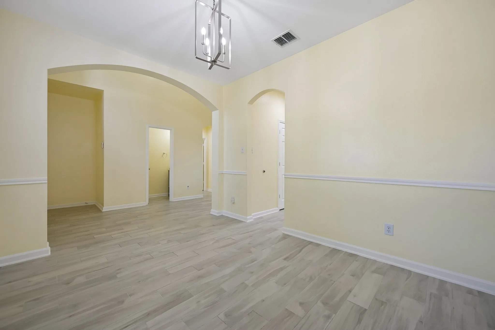 Arched doorways, wood-look tile, chair rail molding, and a modern chandelier