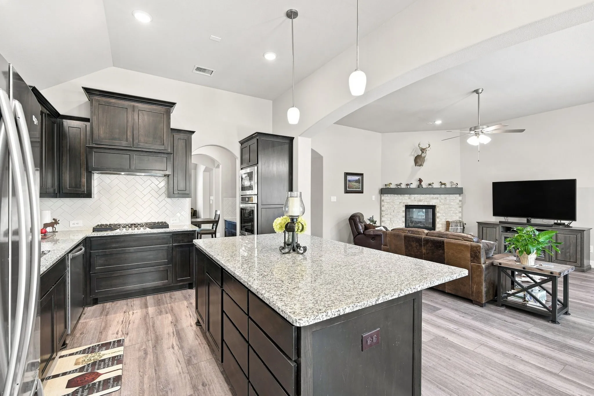 Open-concept kitchen featuring an oversized island, dark wood cabinetry, and subway tile backsplash