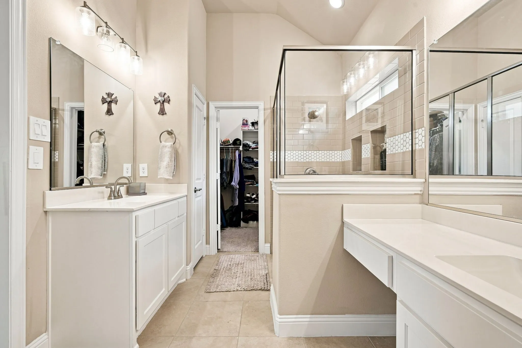 Dual vanities with white cabinetry and integrated sinks, large mirrors, a walk-in shower with glass enclosure, tiled walls, and a recessed window