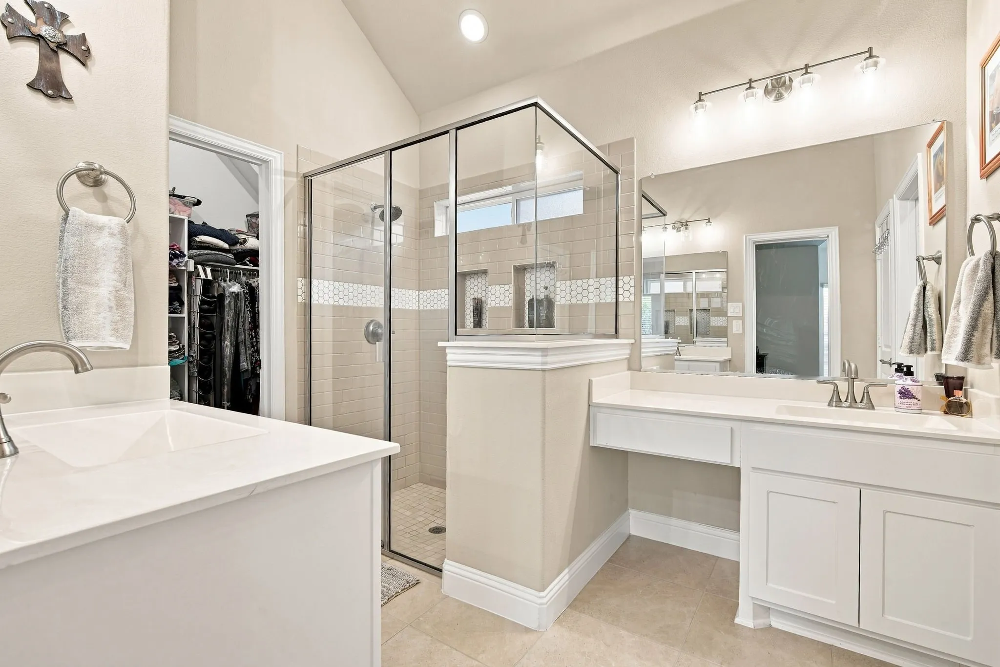 Dual vanity with white cabinetry, built-in makeup counter, and a large frameless mirror