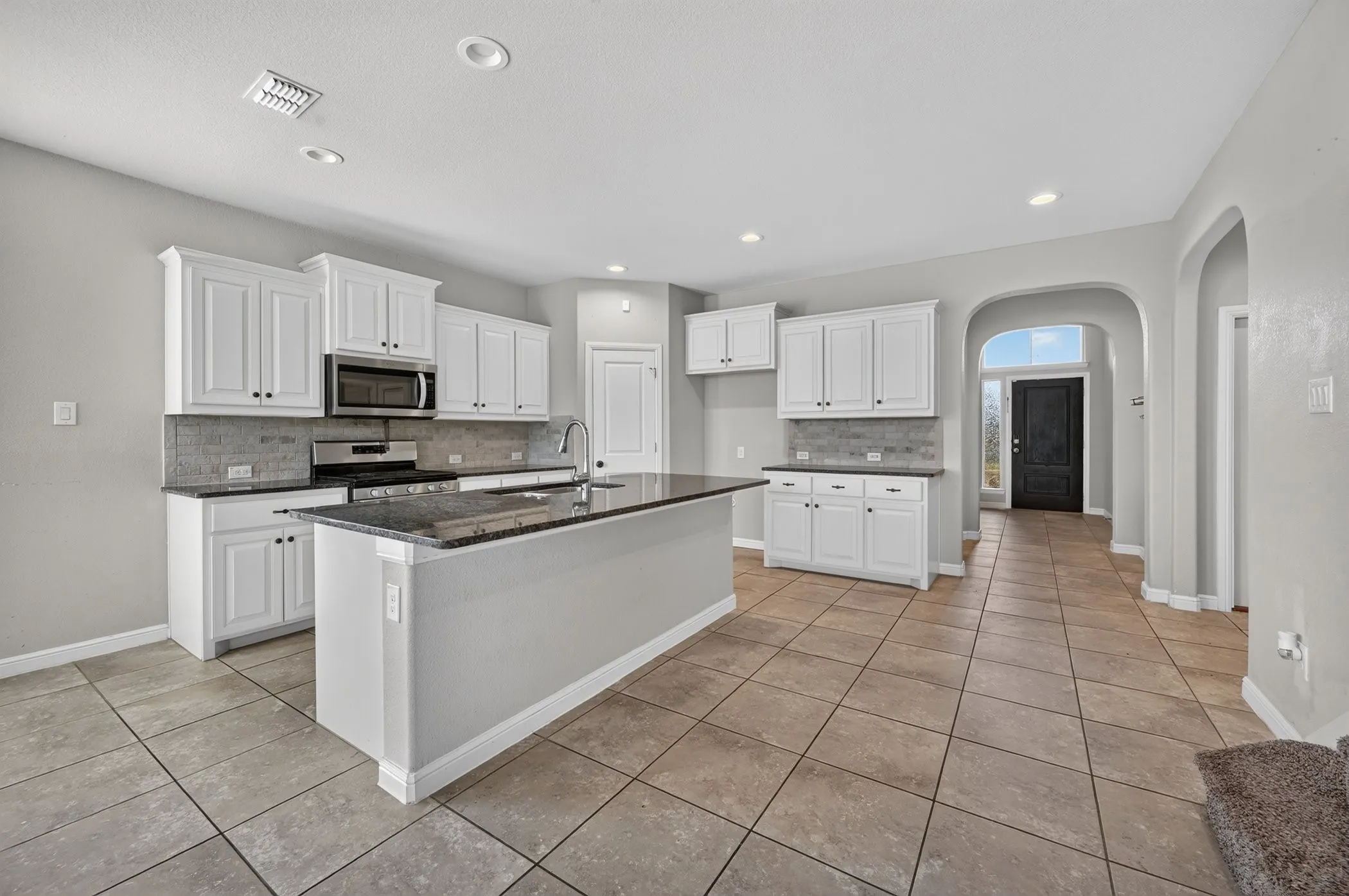 Contemporary kitchen featuring an island with a sink, white cabinetry, dark countertops, tile flooring, and stainless steel appliances