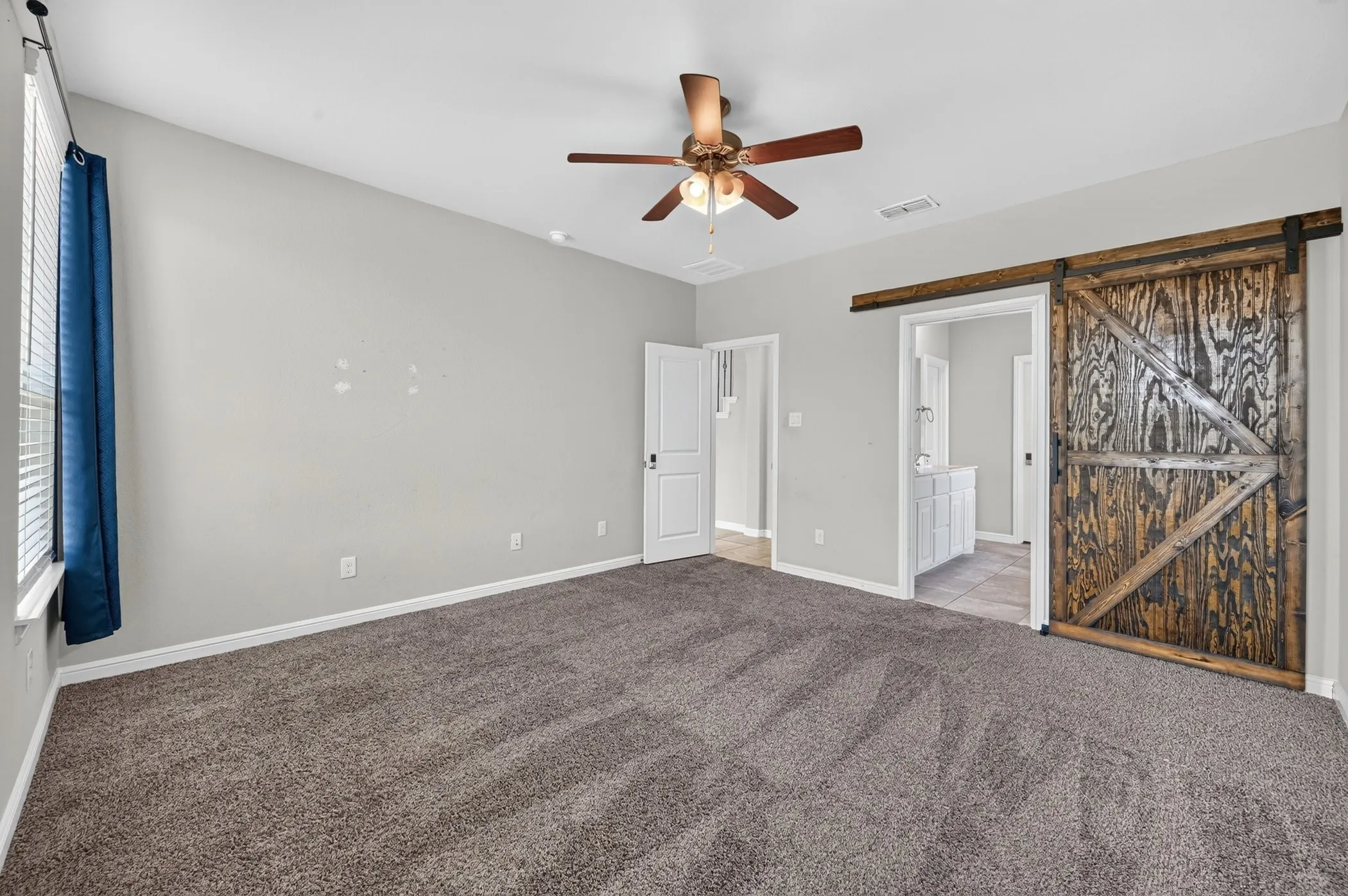 Vaulted ceiling with a ceiling fan, gray carpet, white interior doors, and a wood-finish barn door