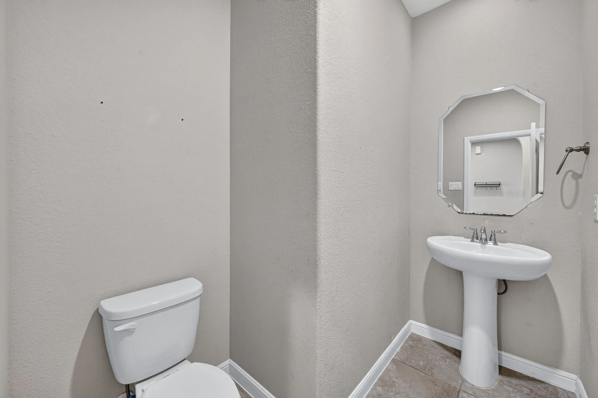 White pedestal sink, tile flooring, wall-mounted mirror, and a two-piece toilet