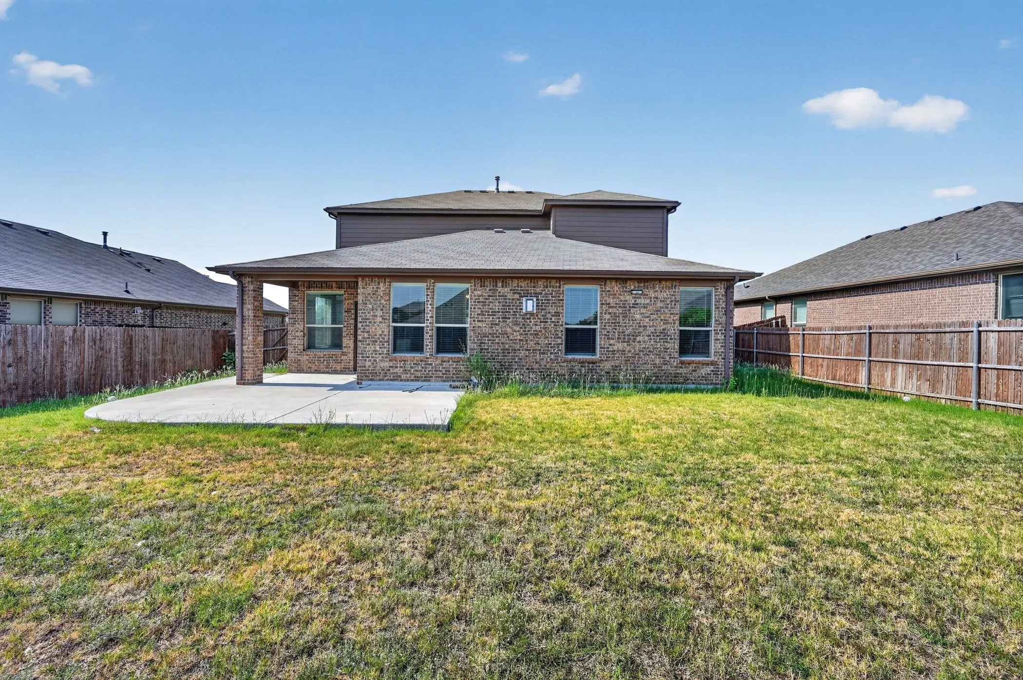 Brick exterior with a covered concrete patio and multiple windows