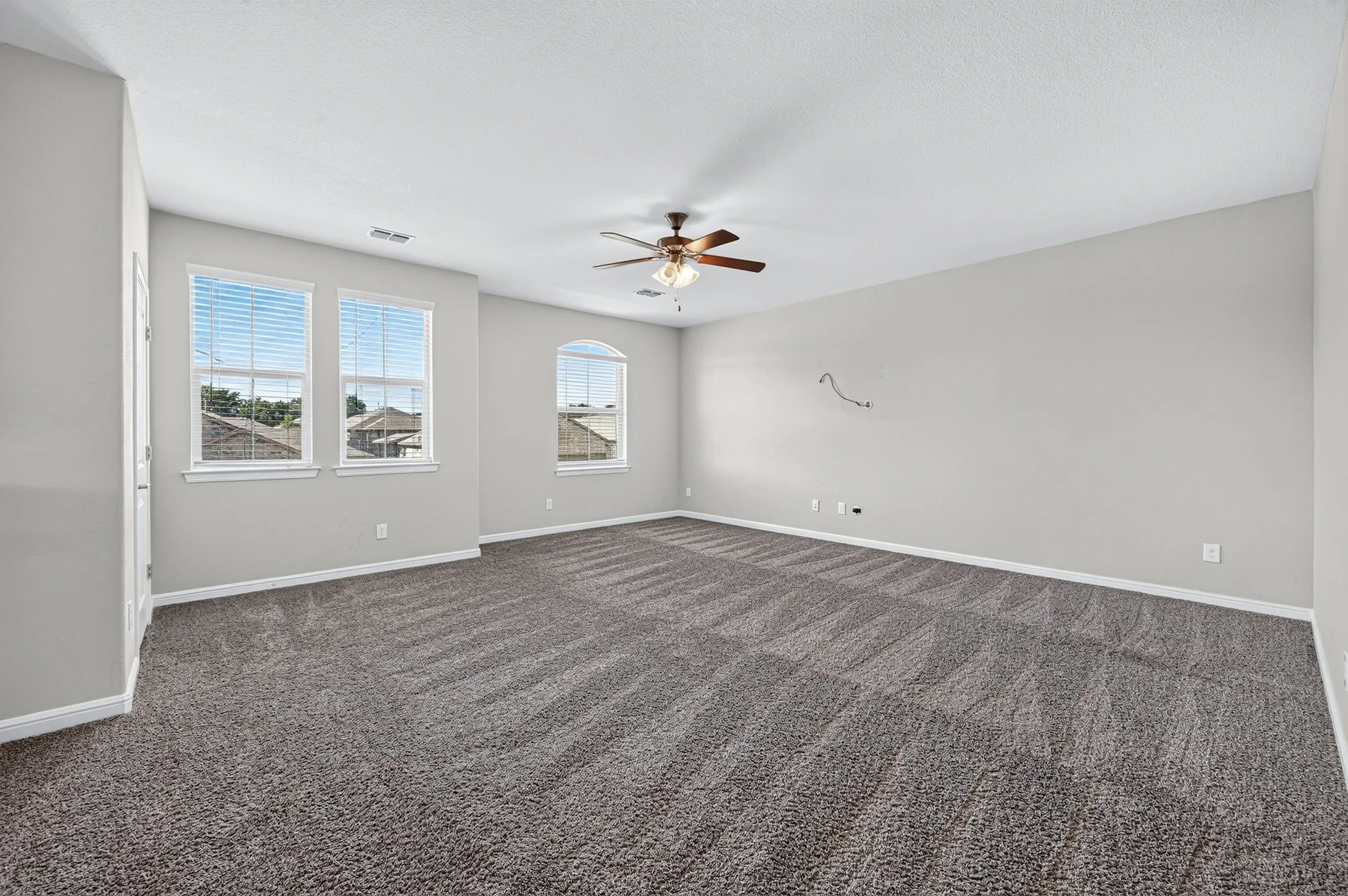 Spacious room featuring gray carpeting, multiple windows, and a ceiling fan