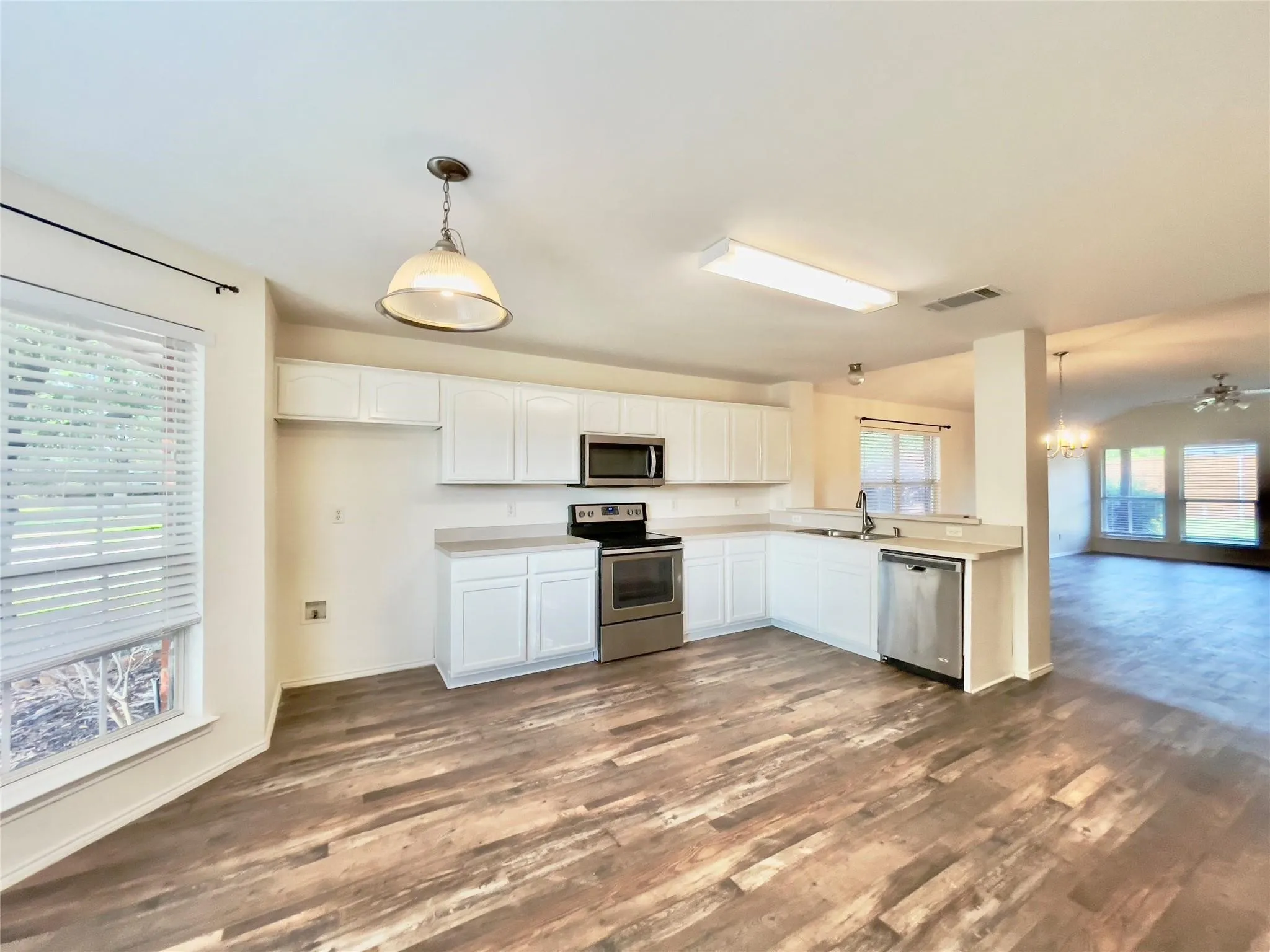 Kitchen featuring white cabinetry, stainless steel appliances, wood-finish flooring, and a peninsula countertop