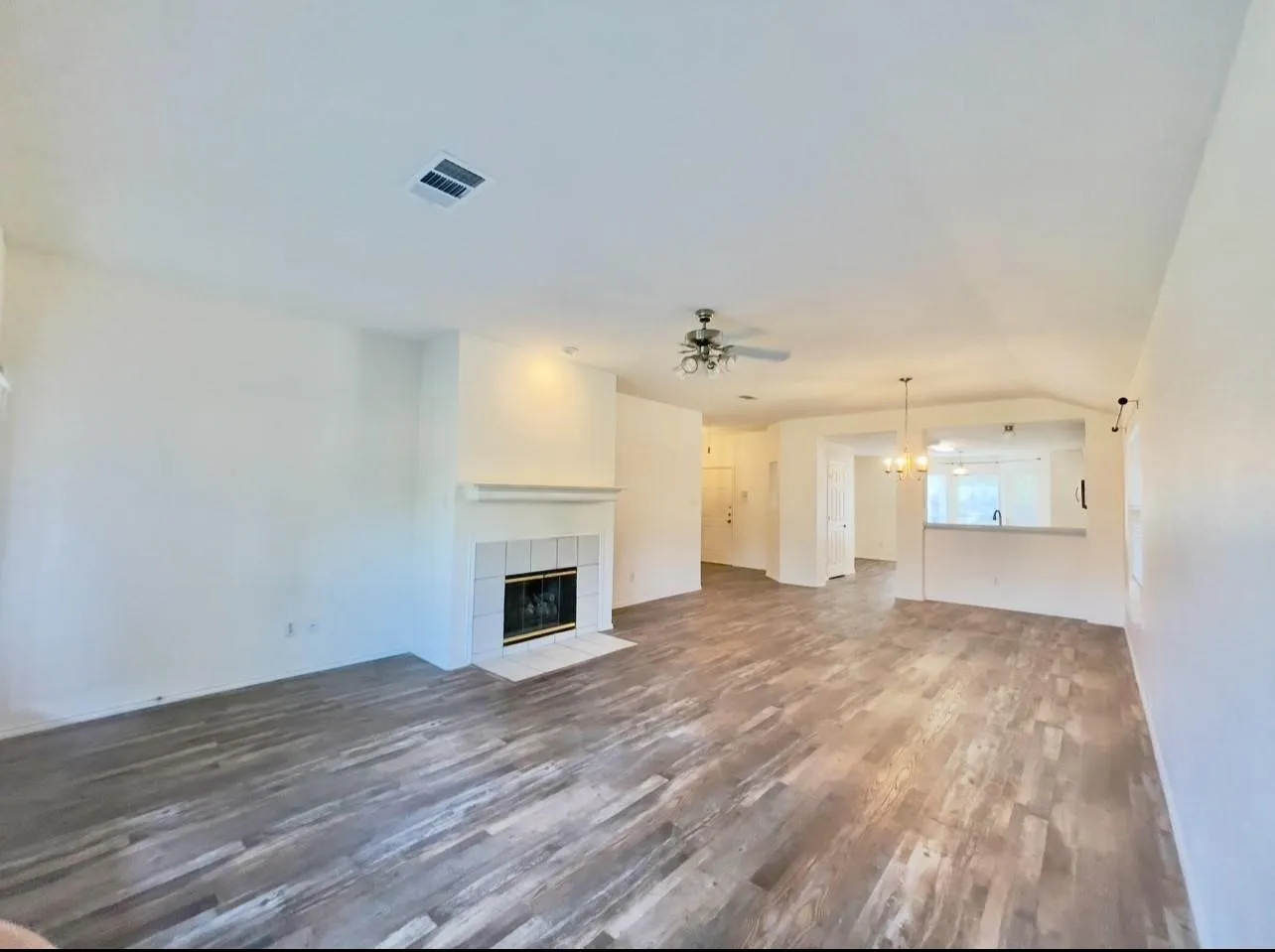 Living area featuring wood-finish flooring, a fireplace with a white tile surround and hearth, and a ceiling fan