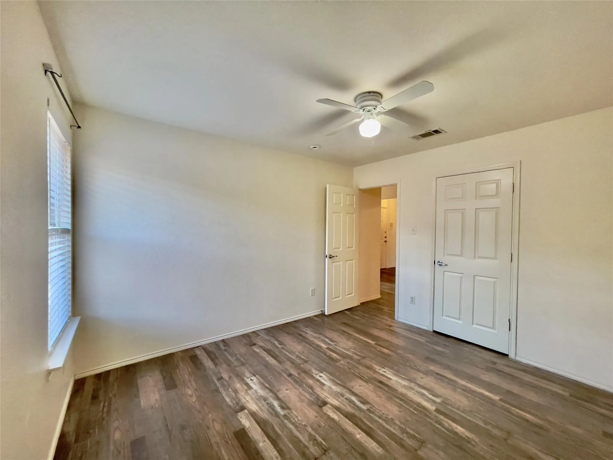 Wood-finish flooring, ceiling fan with integrated lighting, window with horizontal blinds, white paneled doors, and light-toned walls