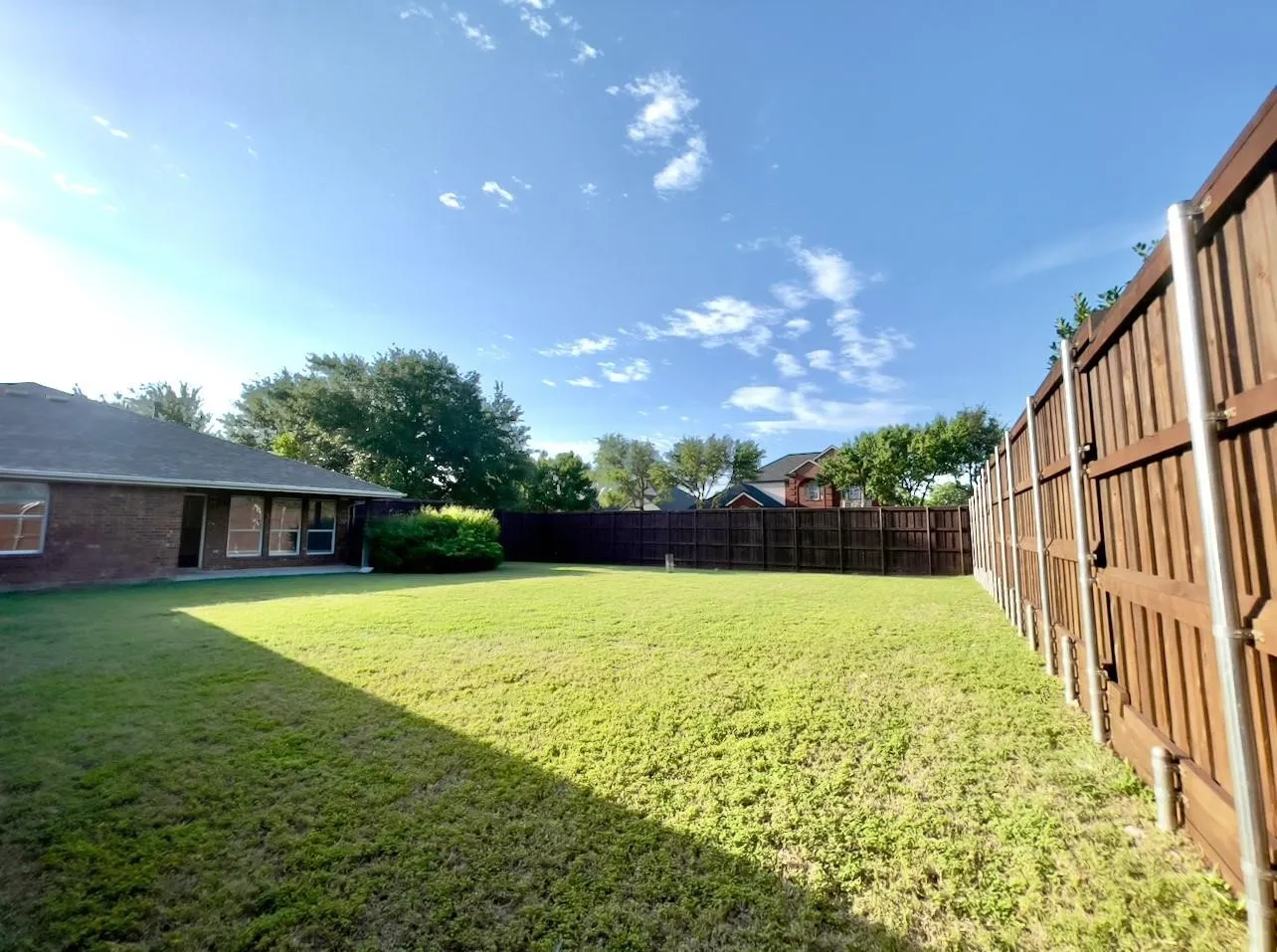 Expansive fenced backyard with a manicured lawn, established landscaping, and a brick-clad exterior