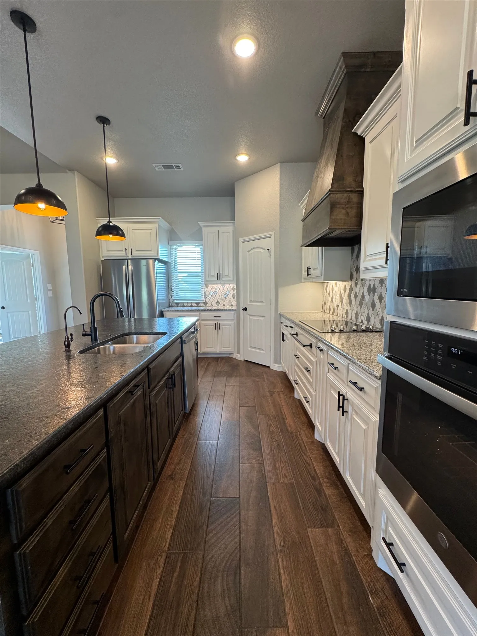 Kitchen featuring wood-finish flooring, two-tone cabinetry, stainless steel appliances, and pendant lighting